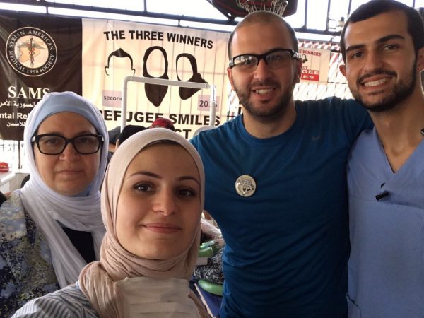 (L-R) Layla Barakat, Suzanne Barakat, Farris Barakat, and Yousef Abu-Salha at the Project Refugee Smiles clinic, at Al Salam School, in Reyhanli, Turkey. The Our Three Winners banner hangs behind them.