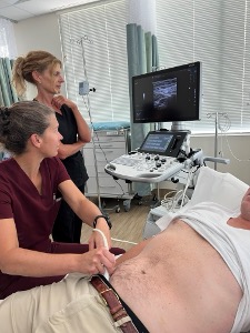 A doctor using gliding an ultrasound probe over a male patient's belly.